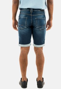 Shorts in denim di un lavaggio scuro con risvolti. Presentano tasche posteriori e dettagli di cucitura. Abbinati a sneakers nere.