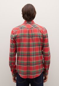 Camicia a quadri rossa con linee verdi e gialle, design con bottoni, maniche lunghe e orlo curvo nella parte inferiore.