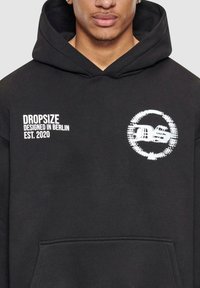 Svart hettegenser laget av mykt materiale med en frontlomme, hvit grafisk tekst "DROPSIZE", og et rundt logo.