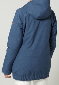 Niebieska kurtka z kapturem wykonana z teksturowanej tkaniny, z regulowanym sznurkiem i lekko dopasowaną talią. Logo umieszczone na lewym rękawie.