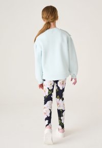 Mintgroene sweatshirt met pofmouwen; gecombineerd met zwarte leggings met een grote bloemenprint en witte sneakers.