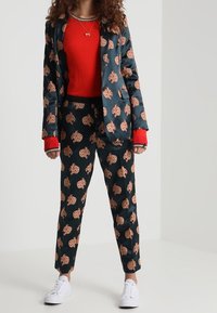 Traje de dos piezas en azul marino con un estampado floral en color melocotón. La chaqueta tiene un cuello de solapa; combinada con un suéter rojo y zapatillas blancas.