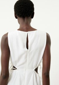 Robe en lin blanc avec un col rond, des côtés dénudés et une taille froncée. Le dos présente une ouverture en forme de clé et une fermeture éclair.