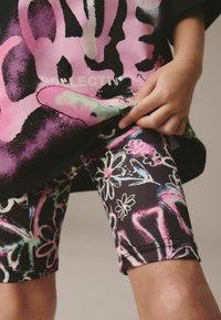 Shorts noirs avec des motifs floraux colorés et des designs abstraits. Le haut est ample, arborant des graphiques audacieux en rose et noir.