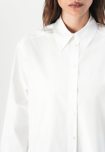 White cotton shirt featuring a classic collar, front button closure, and a smooth texture with a tailored fit.