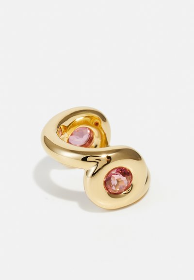 Bague ajustable en ton or avec un design courbé, présentant deux accents arrondis avec des pierres précieuses roses serties à l'avant. Texture lisse et brillante.