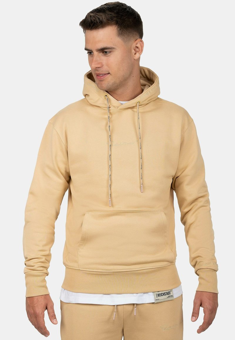 Felpa beige con cappuccio, tasca frontale, polsini a costine e cordini. Presenta dettagli del logo discreti e un tessuto testurizzato.