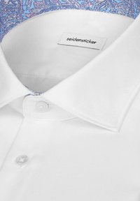 Col de chemise blanche avec boutons blancs et doublure intérieure bleue à motif paisley, portant l’étiquette de la marque « seidensticker ».