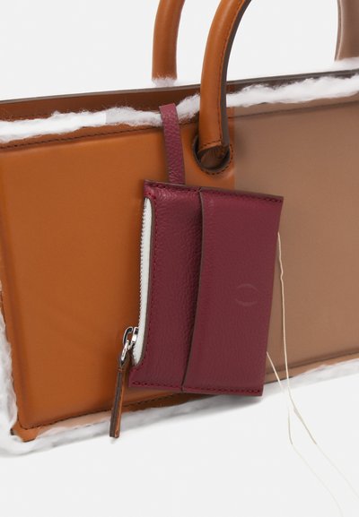 Rjava in prozorna torba z dvema ročkama in pritrjenim burdonskim usnjenim nosilcem za kartice. Opozorljiv bela zadrga in teksturirani materiali.