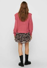 Różowy sweter dzianinowy z bufiastymi rękawami noszony na czarnej spódnicy w kwiatowy wzór. Modelka ma na sobie czarne, masywne, sięgające do kolan botki.