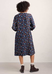 Vestido de color azul marino con estampado floral, de mangas largas, hasta la rodilla, hecho de una tela suave, con flores rojas, azules y amarillas, acompañadas de hojas verdes.
