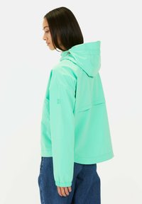 Mintgroene gewatteerde jas met capuchon, elastische manchetten en een relaxte pasvorm, voorzien van een achterzak en een slank, gestroomlijnd ontwerp.