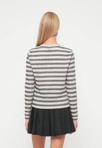 Stripet strikkegenser i grått og hvitt med rund hals. En ribbestrikket tekstur og lange ermer komplementerer et plissert svart skjørt.