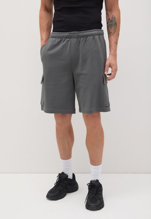 Pantaloni cargo grigi in cotone con vita elastica, tasche laterali e vestibilità comoda, abbinati a sneaker nere e calzini bianchi.