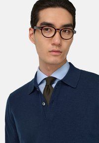 Marineblaues, gestricktes Poloshirt mit spitzem Kragen und Knopfleiste, über einem hellblauen karierten Hemd getragen, kombiniert mit einer grünen Krawatte.