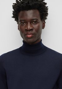 Marinblå polotröja i ett mjukt stickat material. Har en åtsittande design och ribbad textur runt kragen. Snygg yta, minimal detaljering.