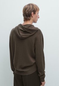 Bruine hoodie van zacht breimateriaal. Heeft ribbelmouwen en een ribbelzoom, met een relaxte pasvorm en subtiele textuur.