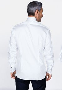 Camicia bianca a maniche lunghe con colletto classico, orlo curvo e polsini con bottoni. Tessuto di cotone liscio con taglio aderente.