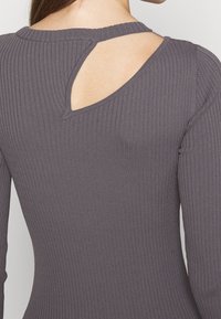Haut à manches longues côtelé en gris foncé avec un détail œillet dans le dos, silhouette ajustée et tissu texturé.