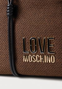 Brown textured fabric handbag featuring black and gold "LOVE MOSCHINO" logo detail, secured with a black cord accent.
