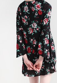 Musta kukallinen mekko, jossa on kellohihat, koristeltu punaisilla ja valkoisilla ruusuilla. Kevyt kangas, rento malli ja ulottuu polven ylle.