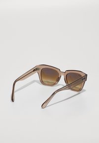 Brune transparente solbriller med gradient brune linser, Ray-Ban-logo synlig på høyre bøyle.