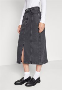 Gonna lunga in denim nero con uno spacco frontale. Presenta un alto punto vita, design a cinque tasche e cuciture a vista. Abbinate a mocassini neri e calzini bianchi.