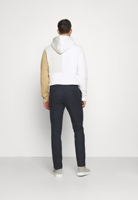 Felpa con cappuccio a blocchi di colore: bianco e beige. Pantaloni slim-fit a scacchi blu navy. Sneakers grigie visibili ai piedi.