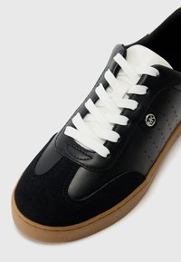 Zwarte leren en suède sneaker met witte veters, gumrubberen zool en geperforeerde details op het bovenwerk. Rondneus ontwerp.