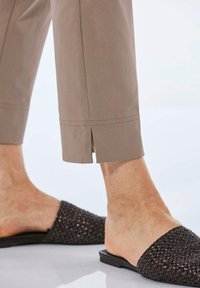 Beige broek met een rechte pijp heeft zijsplitten aan de onderkant. Gepaard met donkergeweven muiltjes, die een gestructureerde bovenkant en platte zool tonen.