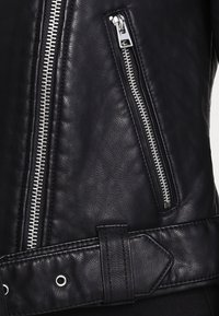 Černá kožená bunda s ozdobnými stříbrnými zipy, opaskem v pase a texturovaným povrchem. Významné detaily zahrnují dvojité boční kapsy a přezku na opasku.