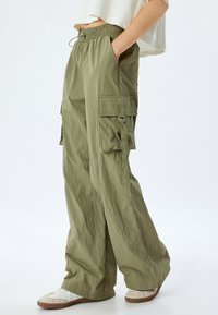 Olivegrüne Cargo-Hose mit weitem Bein, elastischem Bund, zwei Seitentaschen und weichem, strukturiertem Stoff. Mit Cargotaschen an den Seiten.