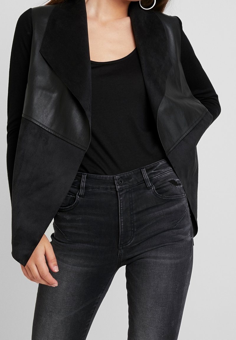 Svart fusk läder och mockastövlett med en öppen framsida, parat med mörka, något slitna högmidjade jeans.
