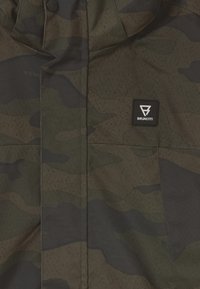 Giacca mimetica in verde scuro e nero, caratterizzata da un tessuto liscio e strutturato e da un patch con il logo Brunotti sulla zona del petto.