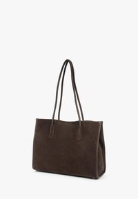 Brązowa zamszowa torba typu tote z dwoma długimi uchwytami, prostokątnym kształtem, płaską podstawą i minimalistycznym wzornictwem. Brak widocznych elementów metalowych ani wzorów.