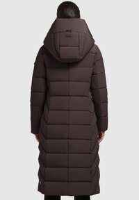 Długa kurtka puchowa w ciemnobrązowym kolorze z pikowanym wzorem, dużym kapturem i zapinanymi na zamek bocznymi kieszeniami. Materiał wydaje się ocieplany i gładki.