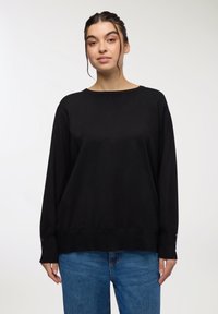 Czarny sweter dzianinowy z długimi rękawami, okrągłym dekoltem i guzikami na mankietach. W zestawieniu z niebieskimi dżinsami. Gładka tekstura.