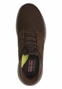 Braune Mesh-Sneaker mit strukturiertem Obermaterial, Schnürdesign, gepolstertem Schaft und einem gelben Akzent an der Innenseite der Ferse. Leichte Sohle.