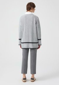 Grijze geribbelde cardigan met zwarte afwerking, gecombineerd met grijze rechte broek. Glad materiaal, lange mouwen en een relaxte pasvorm.