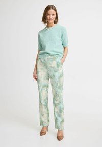 Ljus teal kortärmad tröja med pärlaccents som är kombinerad med mintfärgade och krämfärgade tie-dye raka byxor samt bruna spetsiga klackar.