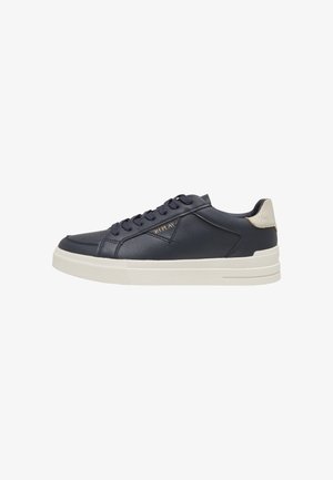 Sort lavtop sneaker med hvid sål, snøredesign, beige hælpude og "REPLAY"-logo i guld på siden.