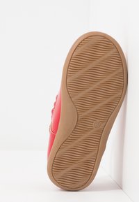 Zapatilla de cuero rojo con detalles texturizados en los laterales y suela de goma, que presenta estrías horizontales para tracción y soporte.