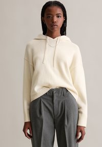 Felpa con cappuccio color avorio con polsini e orlo a coste, abbinata a pantaloni grigi a righe sottili con bottone e pieghe. Design semplice, tessuto strutturato.