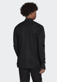Zwarte atletische longsleeve top met een textuurafwerking, voorzien van contrasterende witte strepen langs de mouwen en een opstaande kraag.