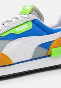 Baskets Puma en bleu, gris et blanc avec des accents orange et vert. Elles présentent une tige texturée et une étiquette de logo distinctive près des lacets.