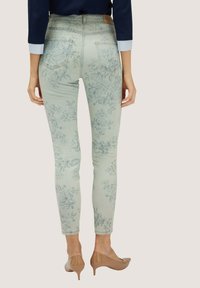 Jeans skinny de flores en azul claro con talle alto, bolsillos traseros y una etiqueta de la marca en la parte posterior, combinados con tacones de aguja nude.