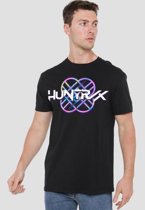 Young man looking right wearing a black T-shirt with colorful geometric design and stylized text "HUNTRX" on the chest.