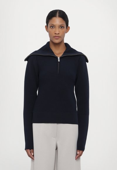 Golf blu navy con zip a un quarto, collo ampio e maniche lunghe. Progettato con una vita aderente e una trama liscia.