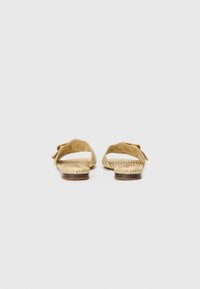 Gold woven sandals with a textured strap design, flat sole, and adjustable buckle. Features natural fiber accents and a smooth inner sole.