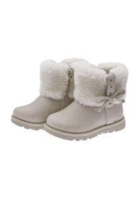 Botas de tobillo beige con suaves puños de piel blanca, cremallera lateral y detalle de lazo en la parte trasera. La tela tiene un acabado texturizado; la suela es de goma con un ligero relieve.